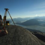 Scott McGee looks out from his survey tripod at the Hole In Wall Glacier from his vantage point above Taku Inlet. The Juneau Icefield Research Program, one of the longest running climate data records in the world, and an outdoor classroom that has trained environmental scientists since 1946.